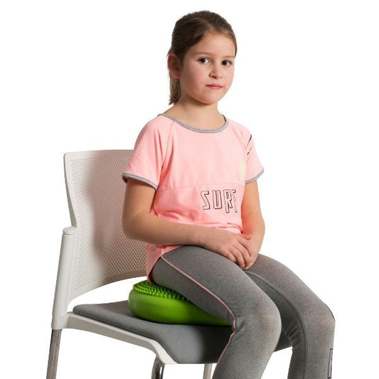 Flicka sitter på taktil kudde för bättre sittställning och fokus i klassrum.