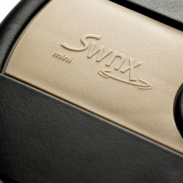 Närbild på SWNX Mini-logotypen präglad på beige och svart fotplatta.