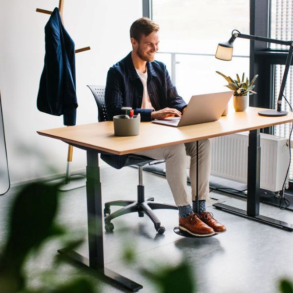 Man arbetar fokuserat vid skrivbord med hjälp av fotgunga för aktivt sittande, SWNX Office monterad under bordet.