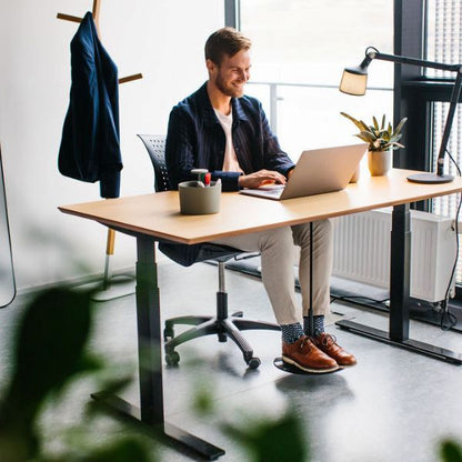 Man arbetar fokuserat vid skrivbord med hjälp av fotgunga för aktivt sittande, SWNX Office monterad under bordet.