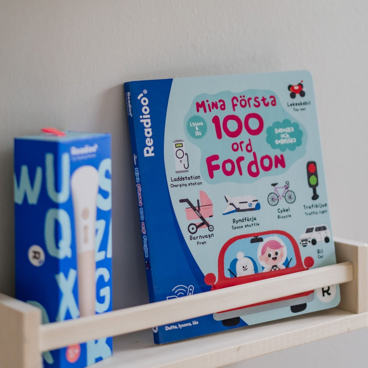 Boken Mina första 100 ord: Fordon från Readioo placerad på hylla bredvid Readioo läspenna.