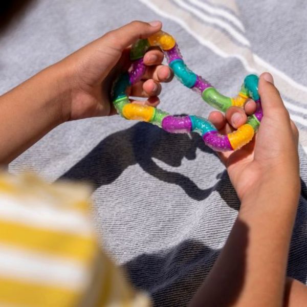 Barnhänder leker med en färgglad Tangle BrainTools Think på en filt.