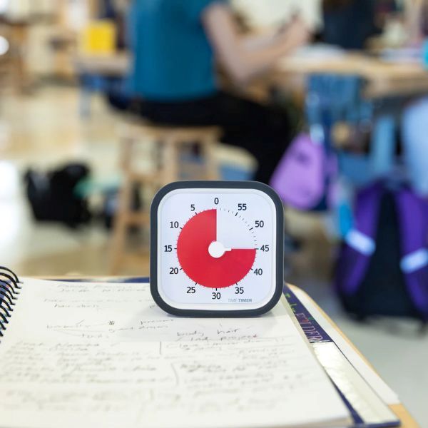 Time Timer MOD placerad på ett skrivbord i ett klassrum, omgiven av anteckningar och skolmaterial.