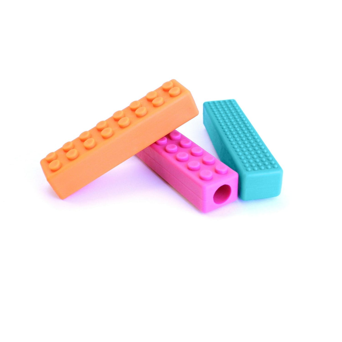Sensoriska tuggpenntoppar i orange, rosa och turkos – brickdesign med taktila strukturer.